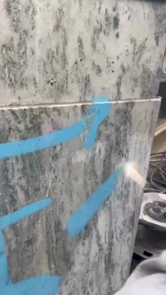 Operario eliminando un grafiti azul de un aplacado de mármol con limpieza láser